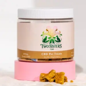 Jar of Two Sisters CBD Pet Treats with some treats in front on a pink platform.