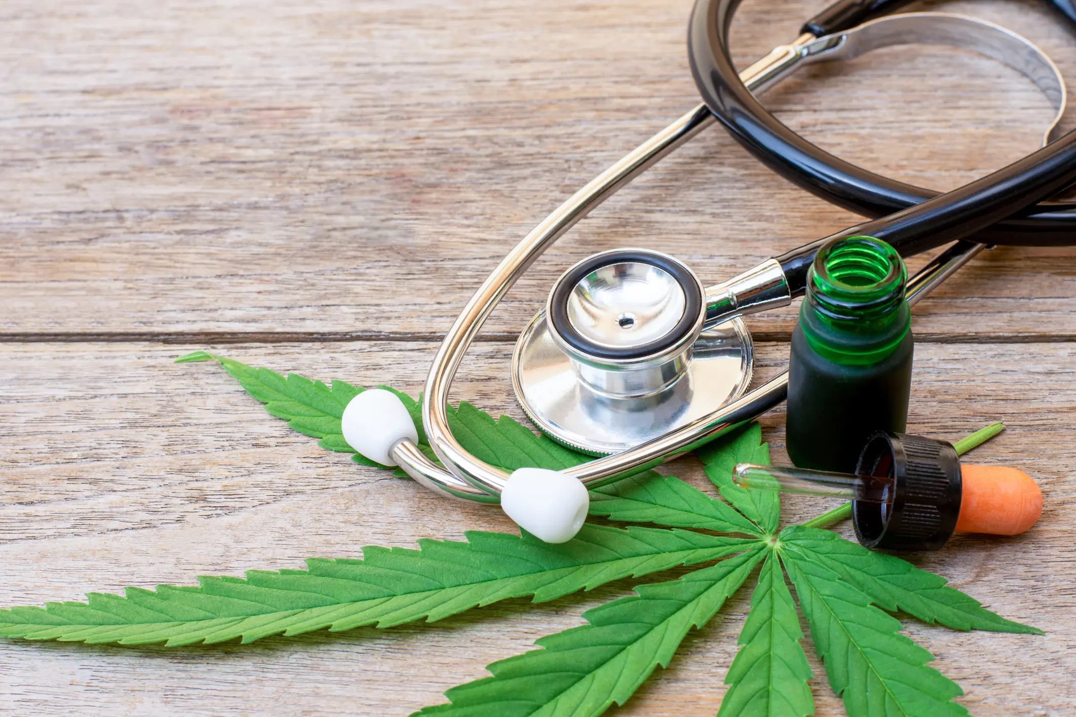 Stethoscope and cannabis leaves with medicine bottles on a wooden surface.