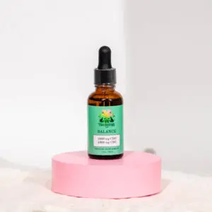 Amber dropper bottle labeled 'CBD Oil' on a pink pedestal against a white background.