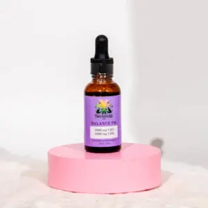 Amber dropper bottle with purple label on pink round pedestal.